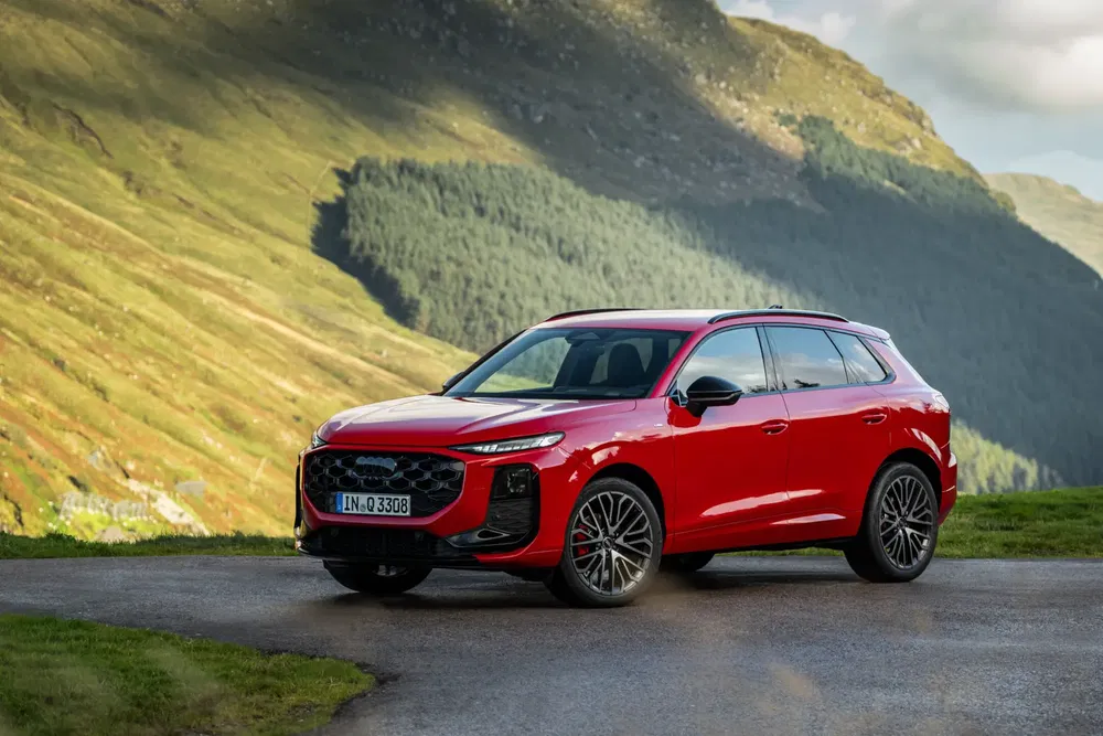 SUV Audi rouge moderne en pleine montagne verdoyante, route sinueuse.