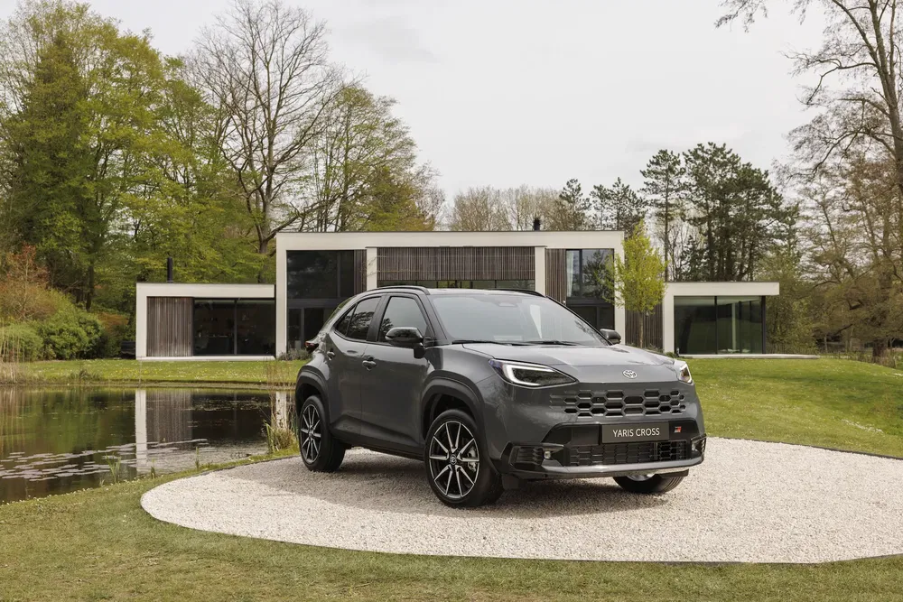 Grijze Toyota Yaris Cross GR voor een modern huis en een rustige vijver.