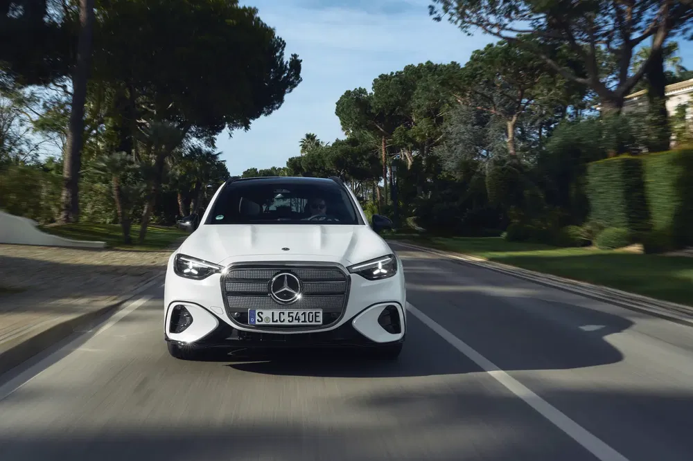 Mercedes-Benz Classe C blanche roulant sur une route bordée d'arbres.