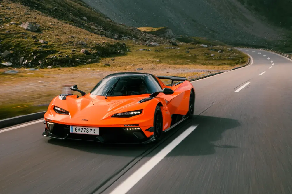 Oranje KTM X-Bow GT-XR sportauto op kronkelige bergweg.