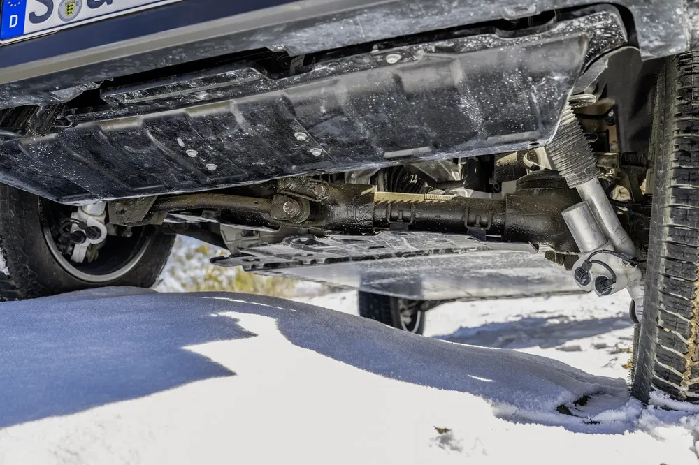 Vue sous un SUV sur neige, montrant la suspension et l'arbre de transmission.