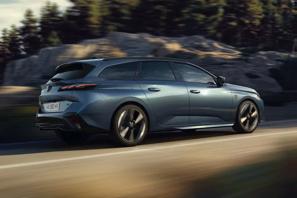 Peugeot 308 SW roulant sur route forestière, profil arrière, design moderne et aérodynamique.
