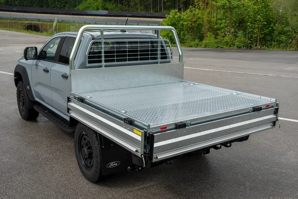 Ford avec plateau arrière utilitaire en métal sur une route goudronnée.