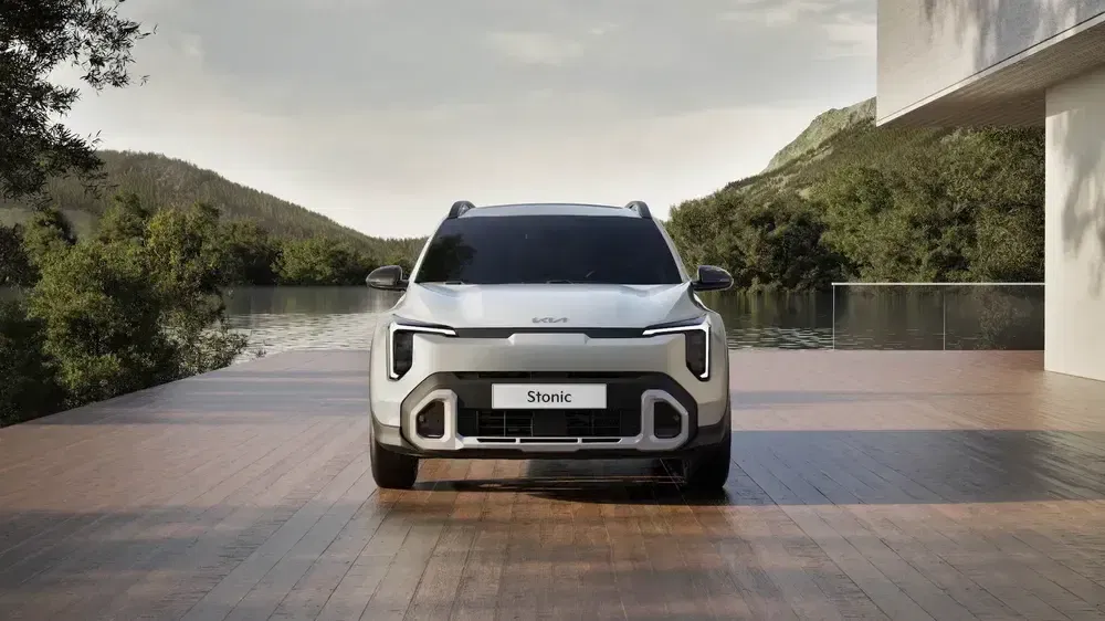 SUV Kia Stonic blanc avant plancher bois, arrière-plan nature verdoyante.