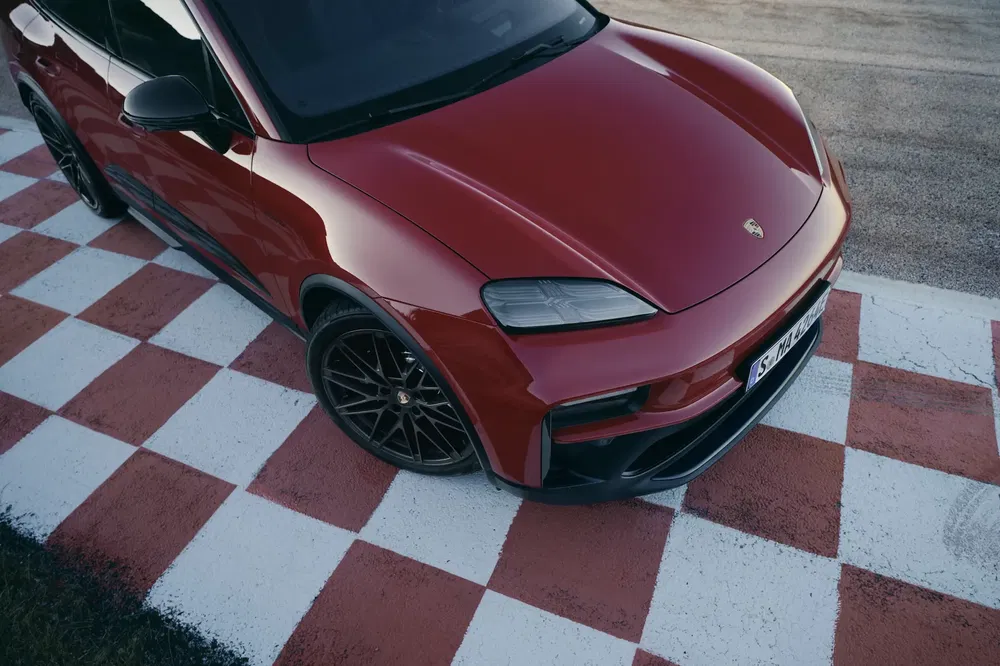 Porsche Macan rouge sur piste à damier, angle plongée, design sportif et moderne.