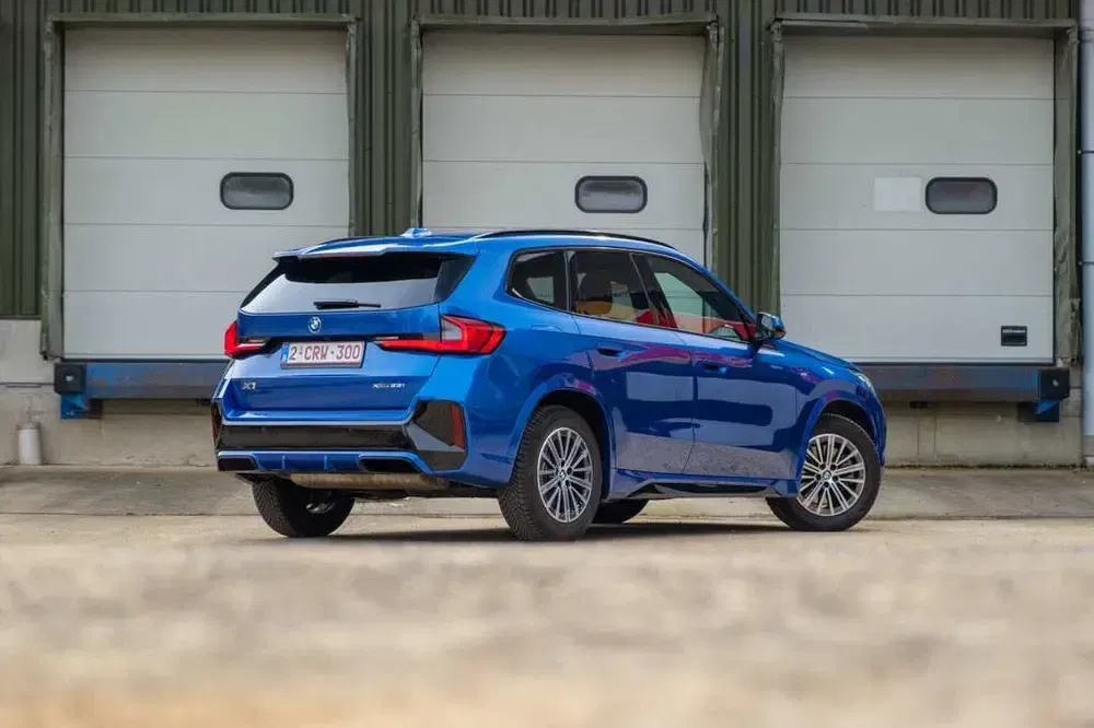 {"fr":"BMW X1 bleu garé devant un bâtiment industriel avec portes blanches.","nl":"Blauwe BMW X1 geparkeerd voor een industrieel gebouw met witte deuren."}