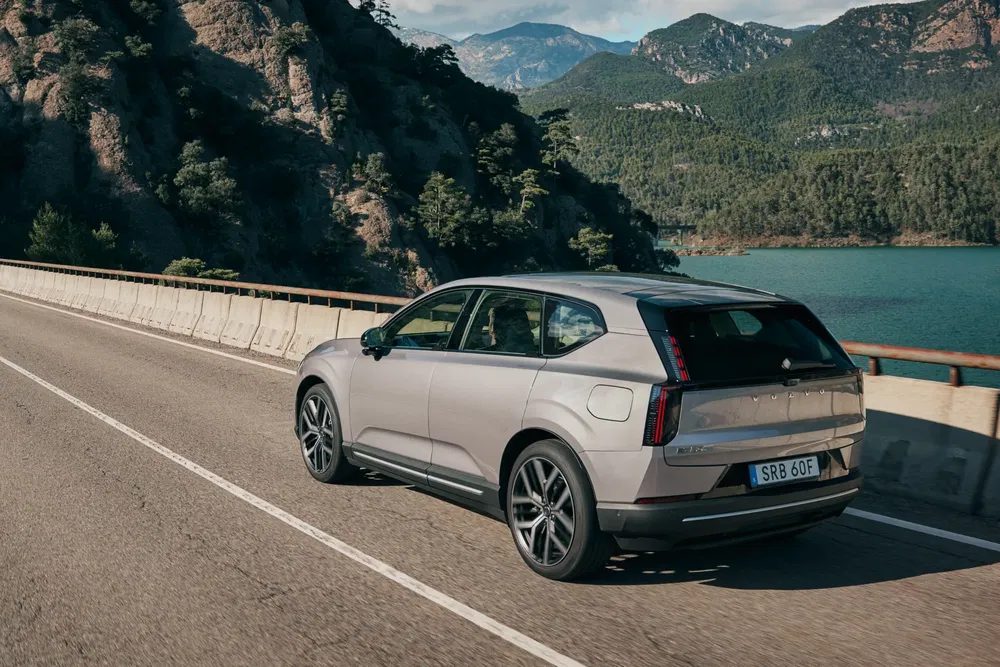 SUV Volvo EX30 roule sur route de montagne pittoresque avec vue sur le lac.
