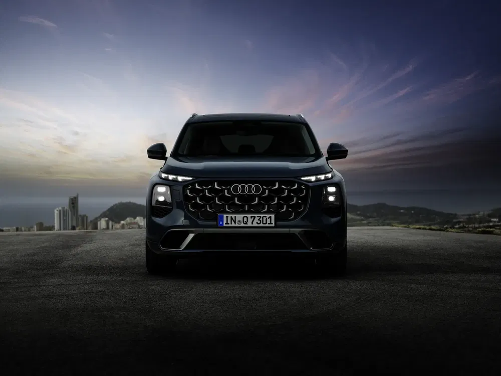 Audi Q7 2023 silhouetté à l'aube, surplombant une ville lointaine.
