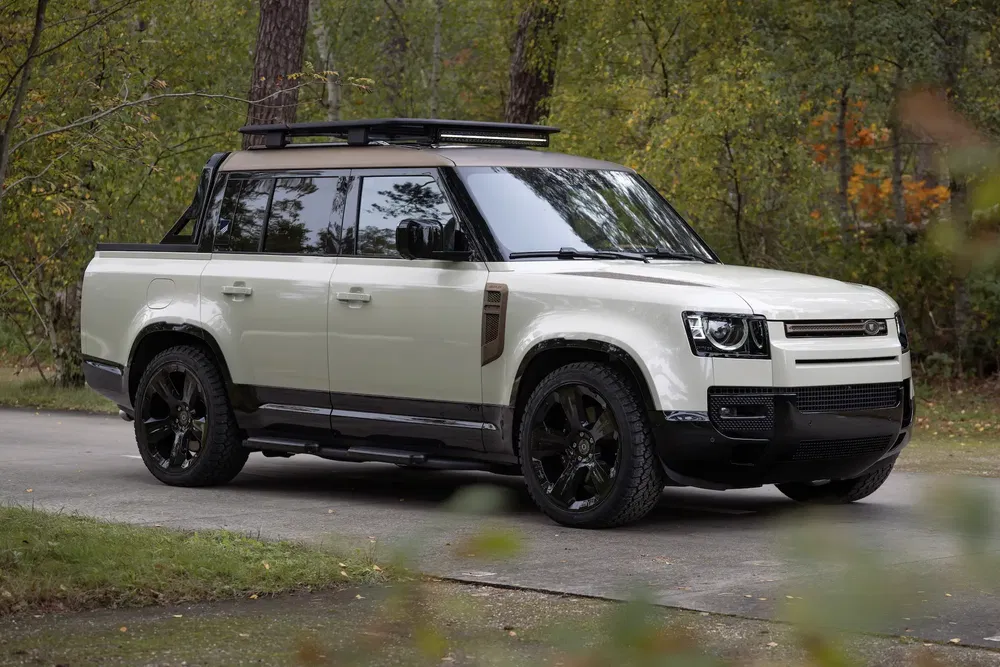 Land Rover Defender moderne, couleur crème, garé dans une forêt, équipé d'un toit porte-bagages.