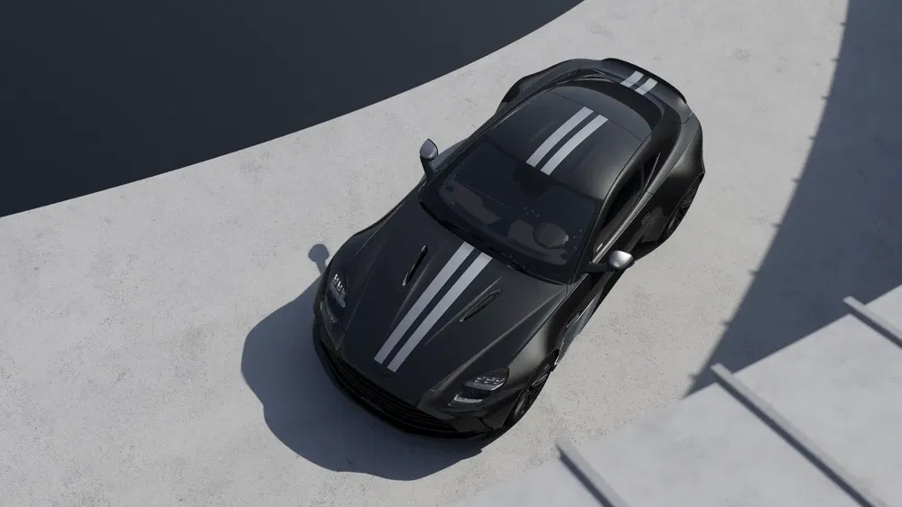 Voiture Aston Martin noire avec bandes blanches garée sur fond de béton clair.