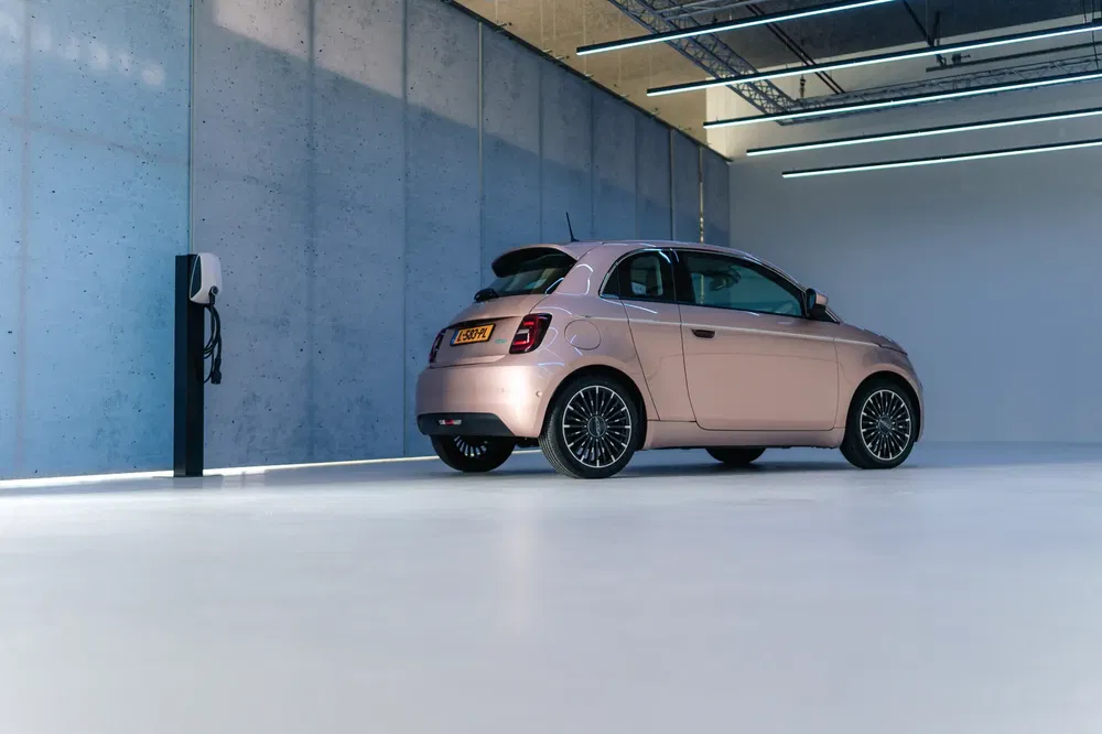 Roze elektrische Fiat 500 geparkeerd in moderne parkeergarage met laadstation.