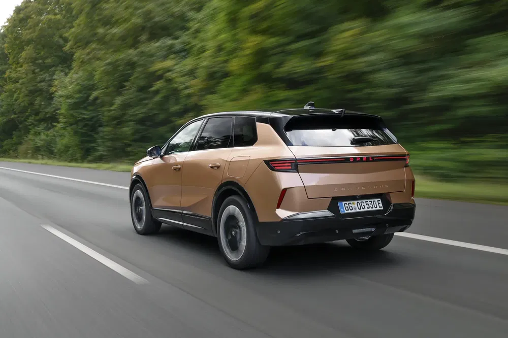 Koperen Opel Grandland SUV hybride rijdt op boomrijke snelweg.