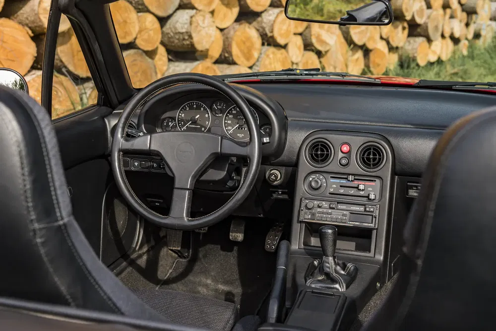 Intérieur d'une Mazda MX-5 vintage avec tableau de bord et volant, fond de bûches.