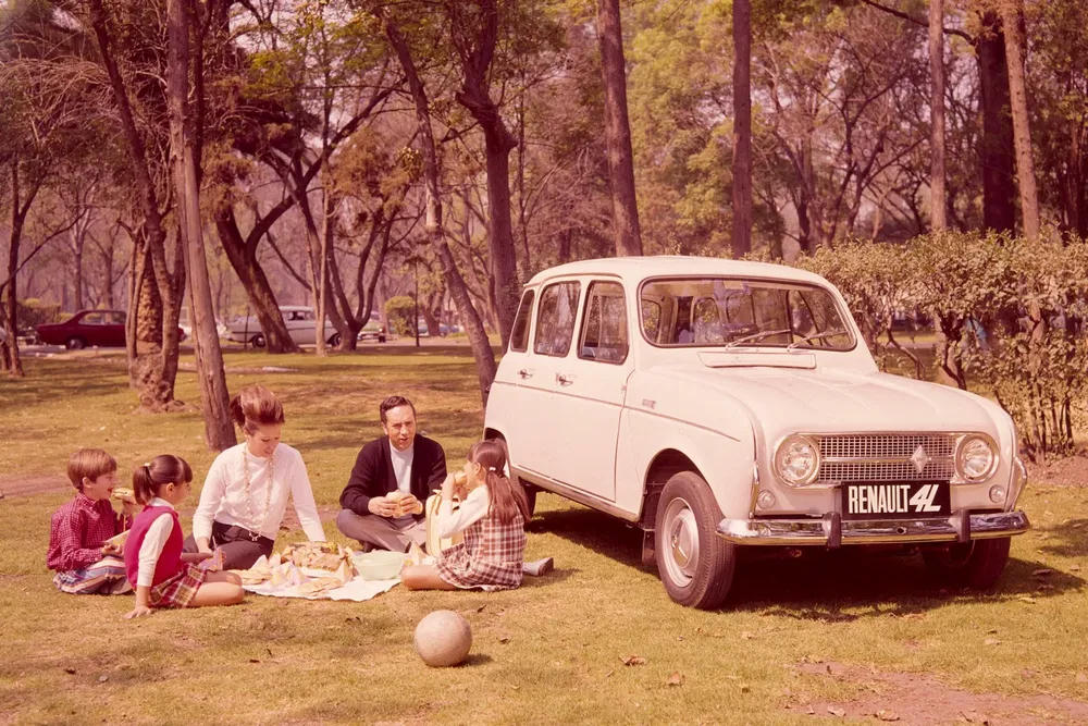 Gezin picknickt naast een witte Renault 4L in een bosrijk park.