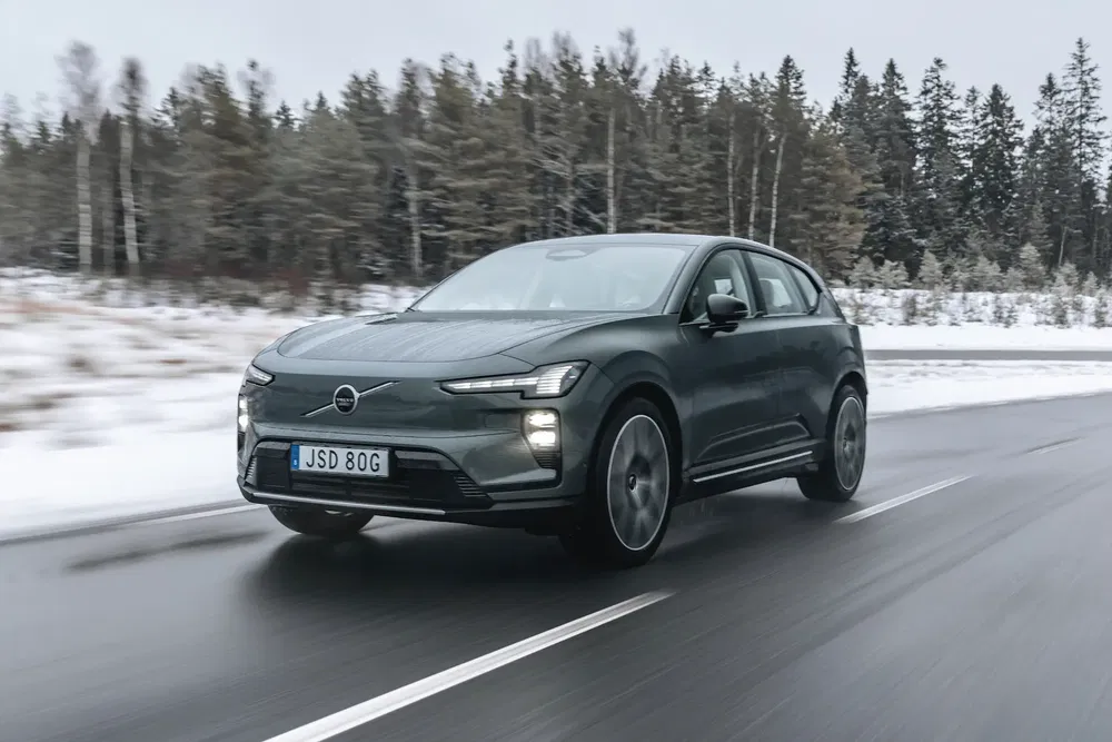 Volvo EX90 roulant sur une route enneigée bordée d'arbres, mettant en valeur son design moderne.