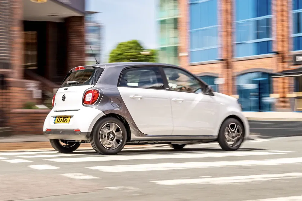 {"fr":"Une Smart ForFour blanche traverse un passage piéton dans un environnement urbain moderne.","nl":"Een witte Smart ForFour rijdt over een zebrapad in een moderne stedelijke omgeving."}