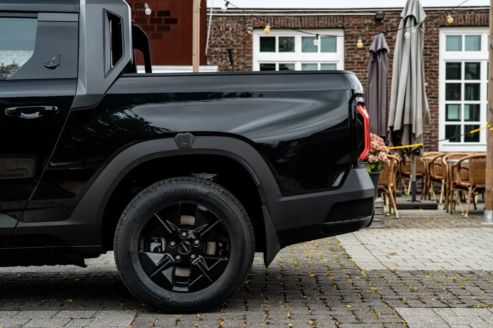 Camion électrique noir Rivian R1T garé devant un café en terrasse en ville.