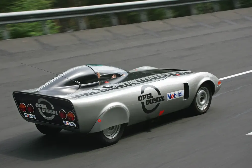 Zilvergrijze Opel Diesel prototype met aerodynamisch ontwerp op het circuit, logo's zichtbaar.
