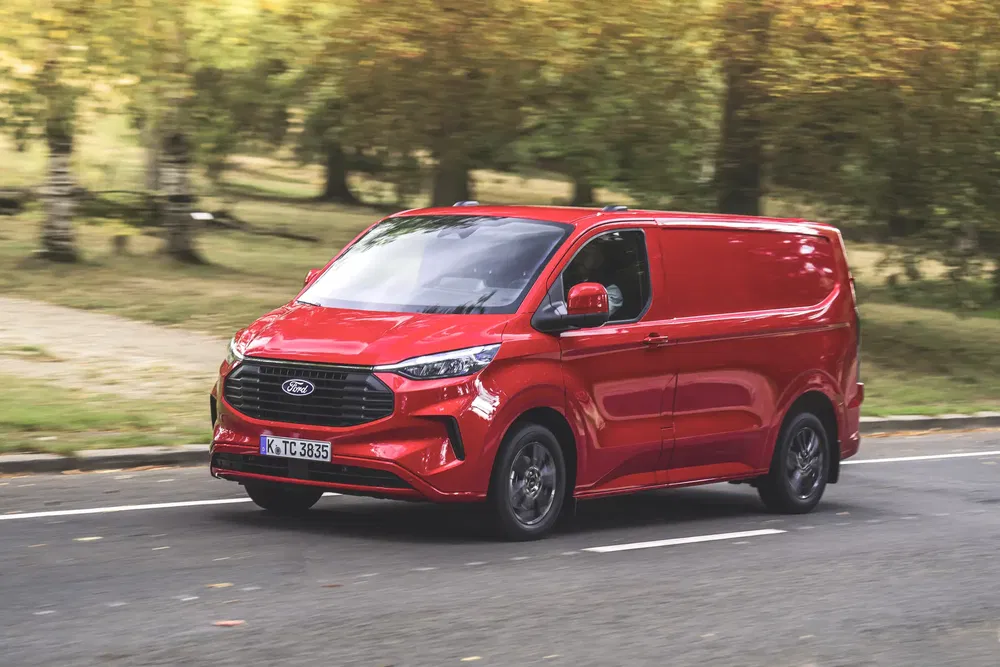 Fourgon Ford Transit Custom rouge roulant sur une route entourée d'arbres.