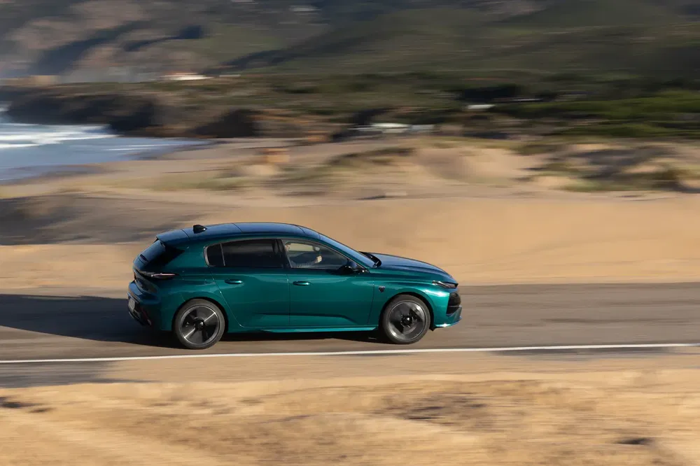 Groene Peugeot 308 rijdt langs schilderachtige kustweg bij helder weer.