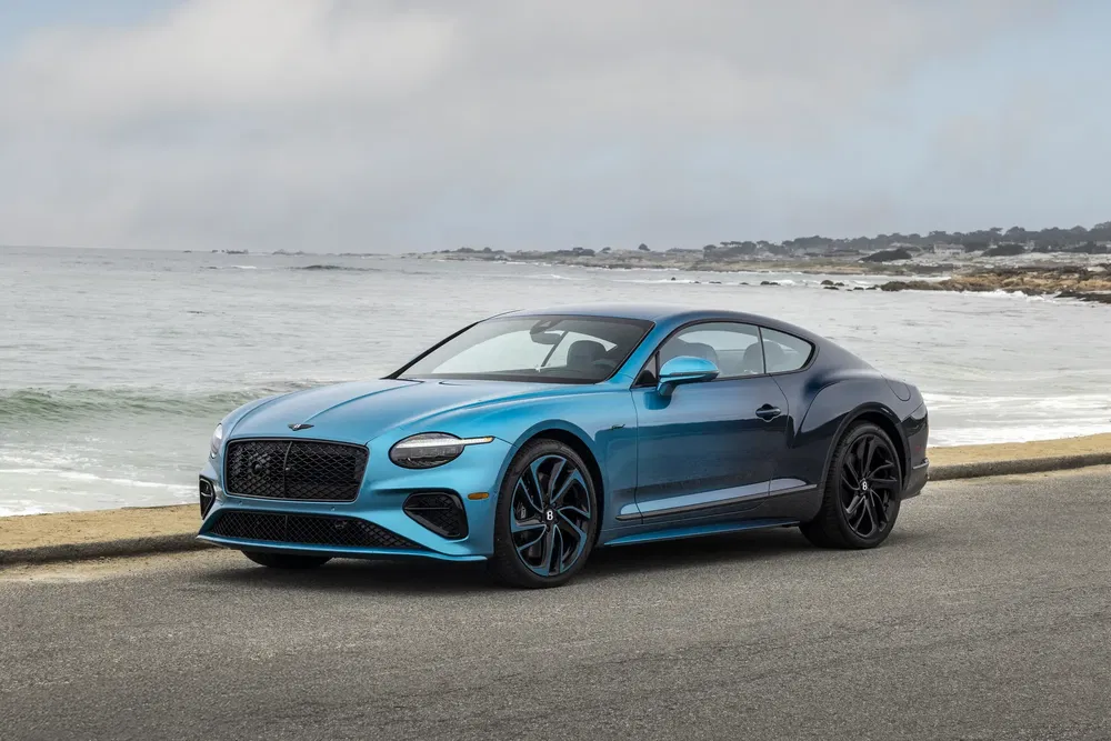 Bentley Continental GT bleue garée au bord de la mer sur une route côtière.