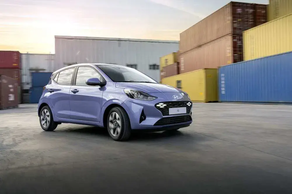 Hyundai i10 bleu devant des conteneurs colorés, sur un site industriel.