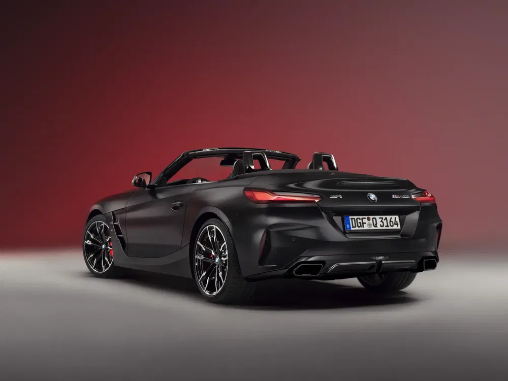 Zwarte BMW Z4 cabriolet, stijlvolle achterkant tegen een rode achtergrond.