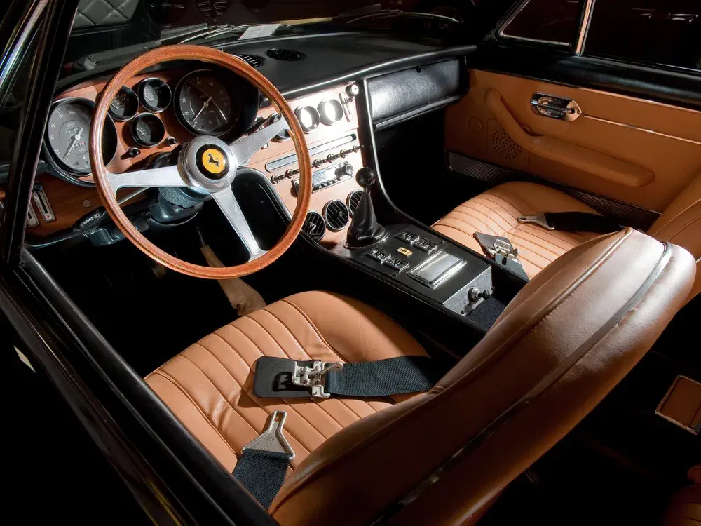 Klassiek Ferrari-interieur met houten stuurwiel en beige lederen zetels.
