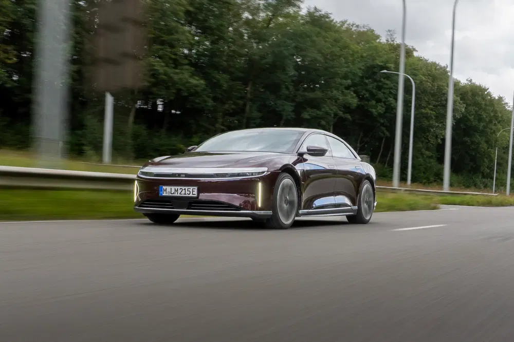 Lucid Air marron sur route, entourée de végétation et lampadaires modernes.