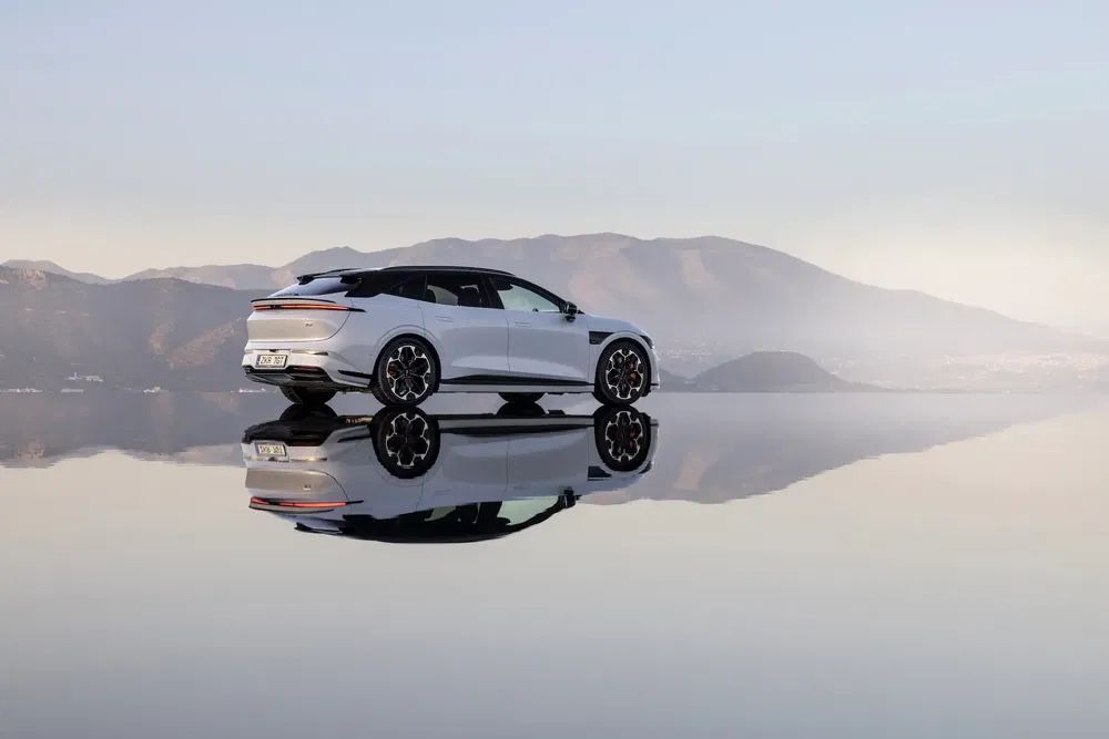 Voiture Lucid Air blanche se reflétant sur une surface d'eau, montagnes en arrière-plan.