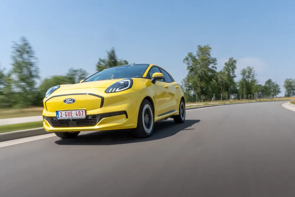 Ford Puma jaune vibrant roulant sur une route bordée d'arbres.