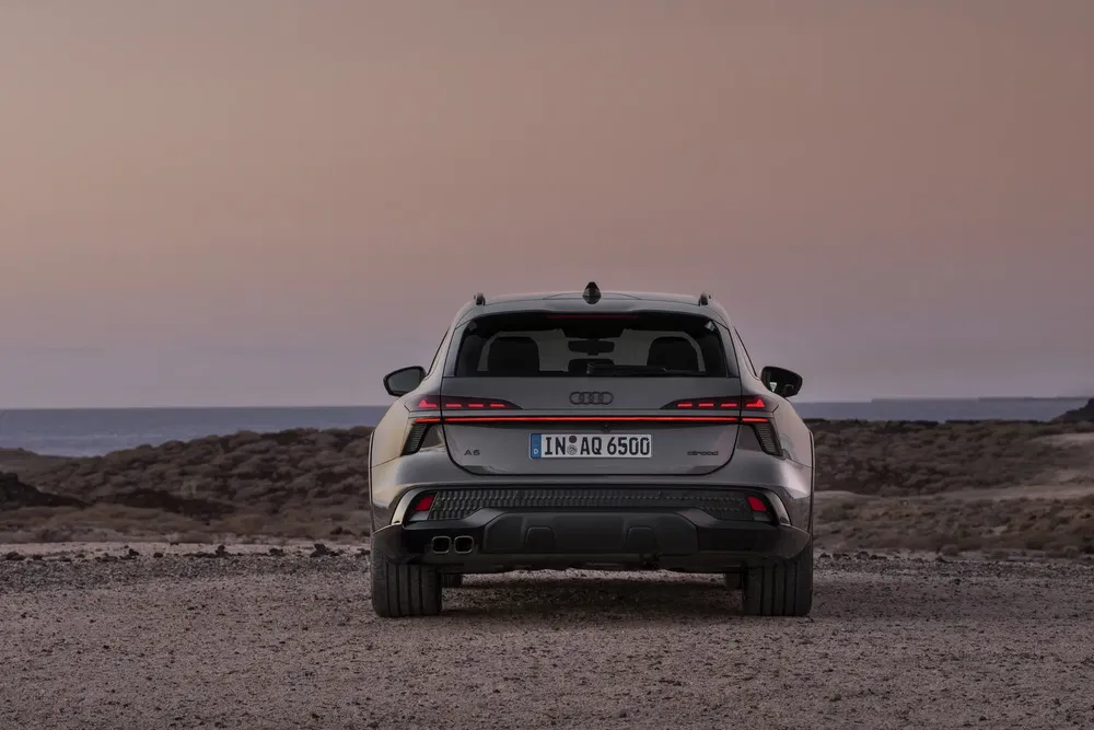 Audi A6 Allroad 2024, achterkant bij zonsondergang op rotsachtig terrein.