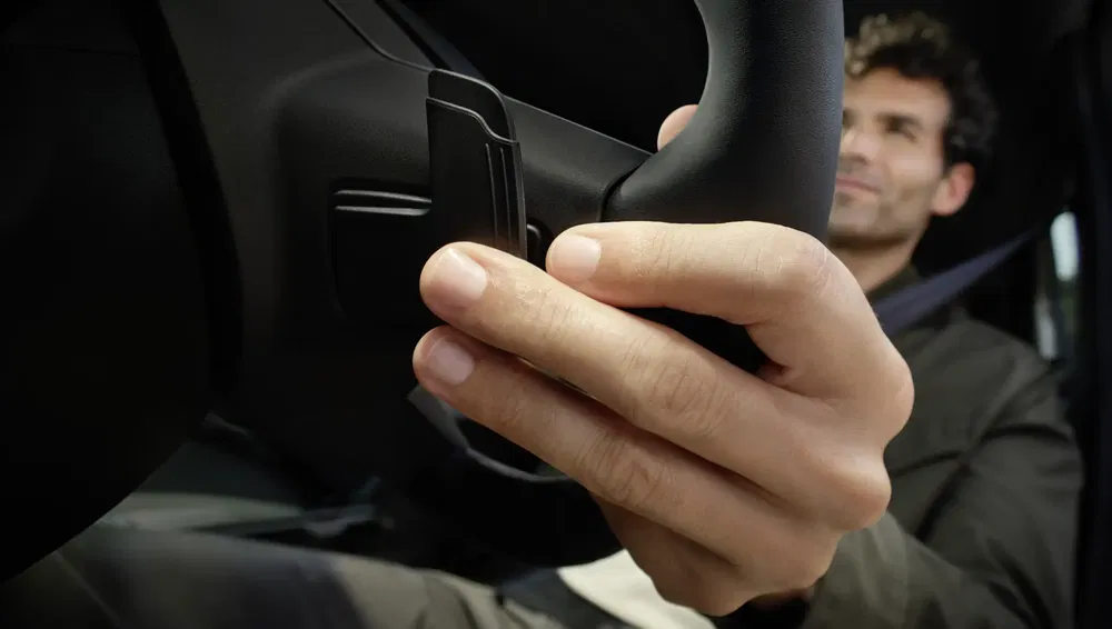Homme tenant un volant avec commande de palettes dans une voiture moderne.