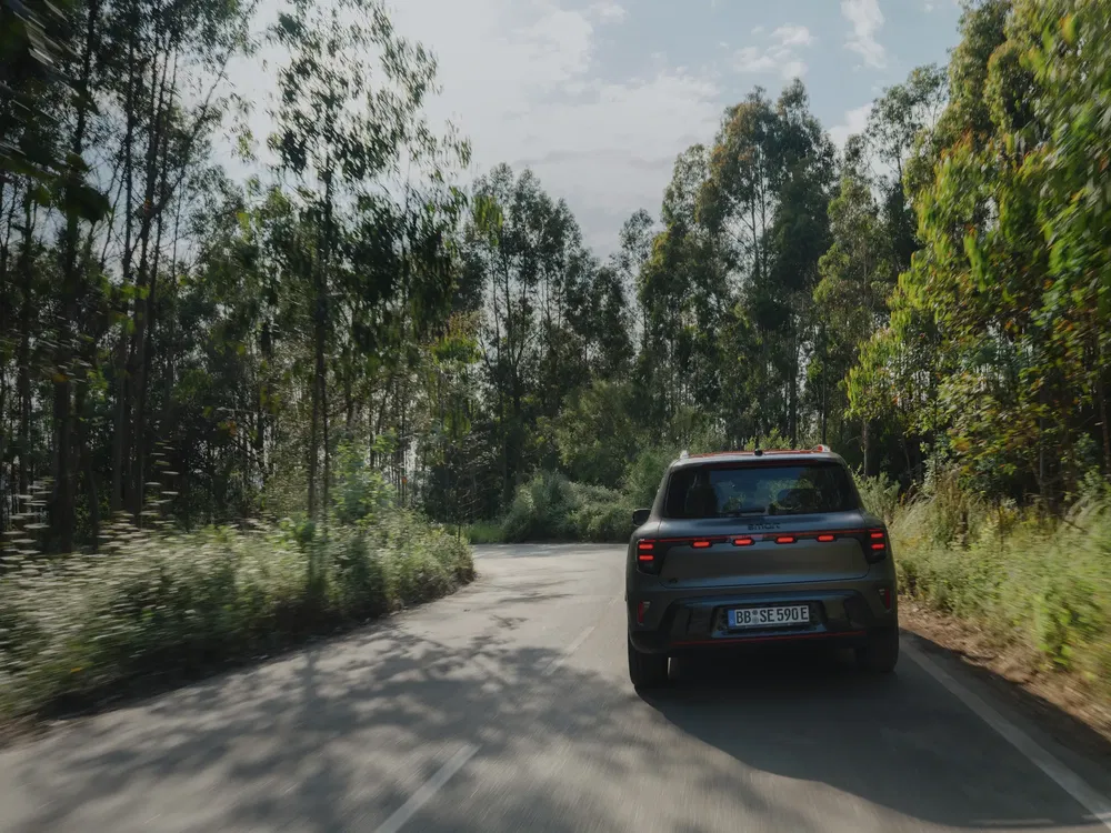 Moderne SUV op kronkelige bosweg onder deels bewolkte hemel.