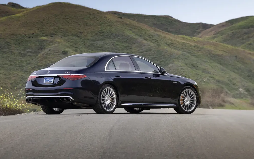 Berline Mercedes-Benz Classe S noire sur route vallonnée pittoresque, arrière élégant et luxueux.