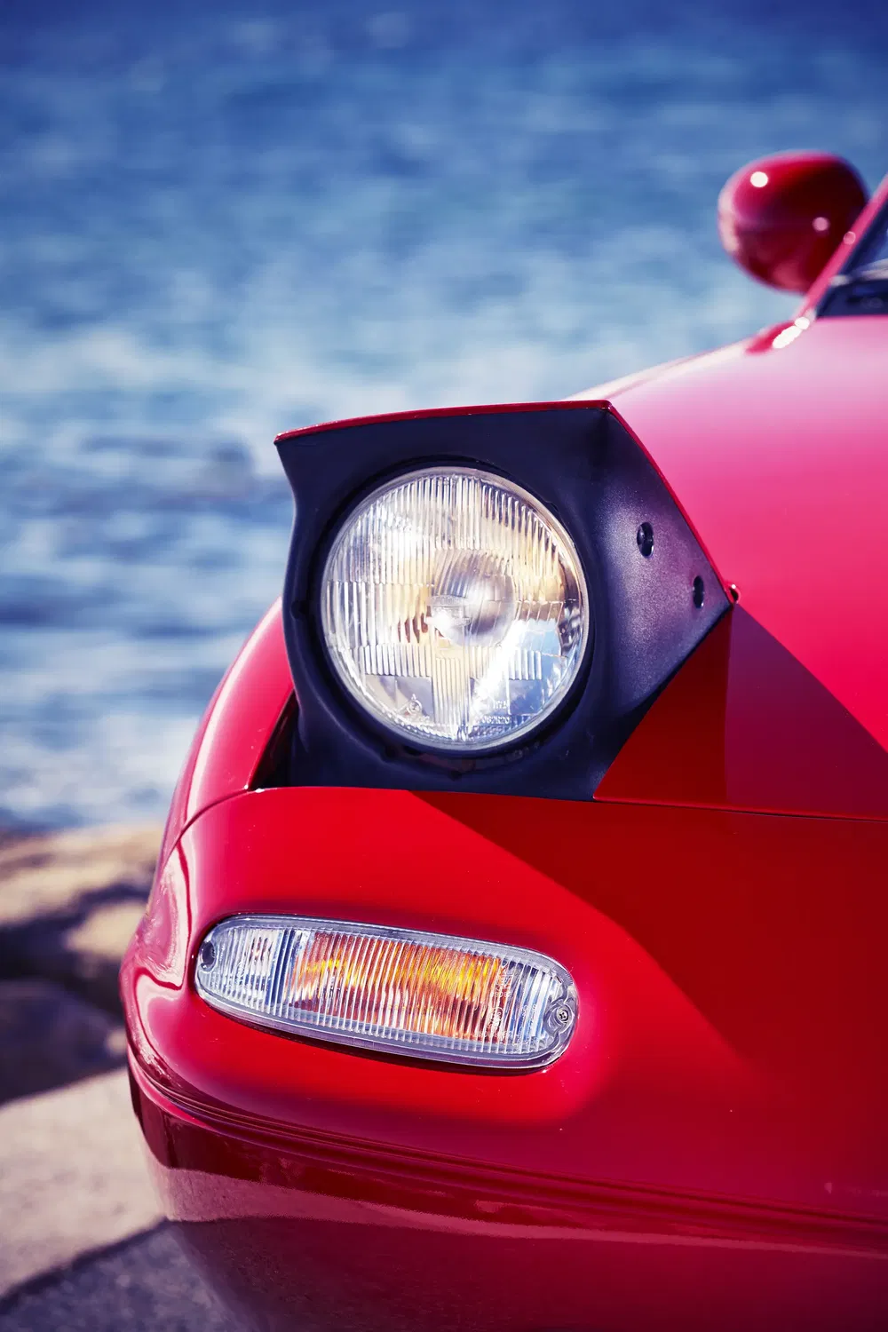 Gros plan du phare avant gauche de la Mazda MX-5 rouge près de l'eau.