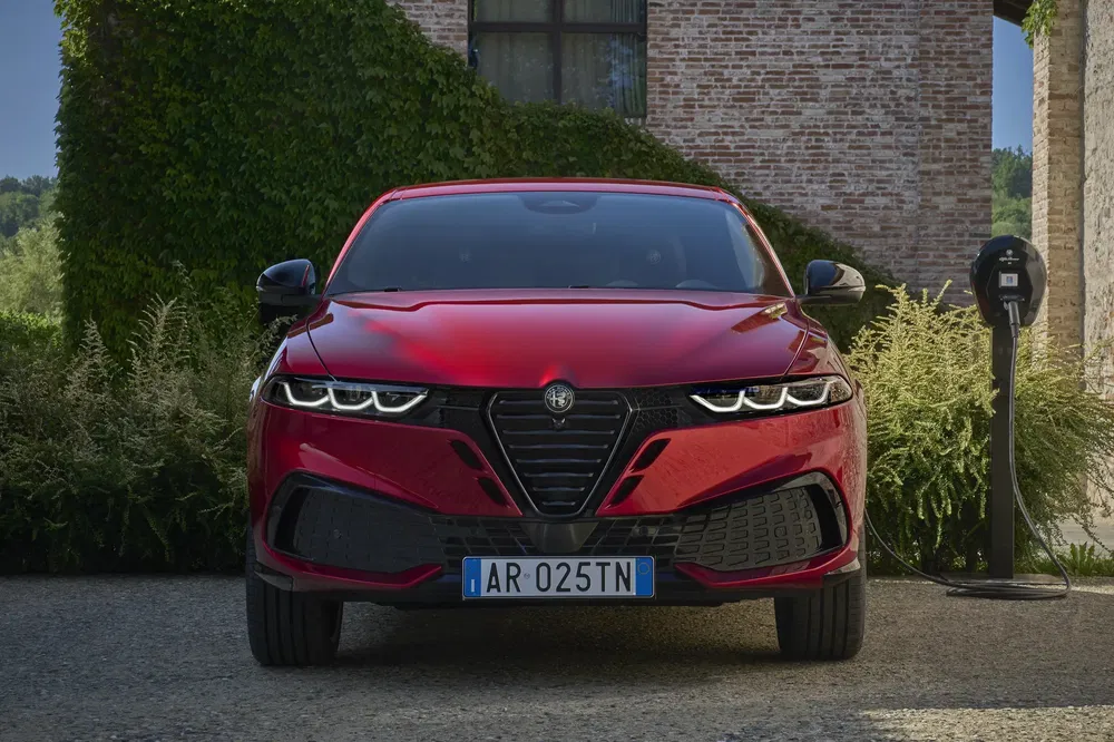Rode Alfa Romeo voor een bakstenen gebouw, laadstation rechts.