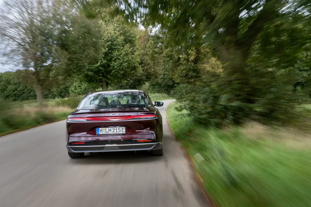 Voiture électrique Lucid Air rouge en mouvement sur route de campagne bordée d'arbres verts.