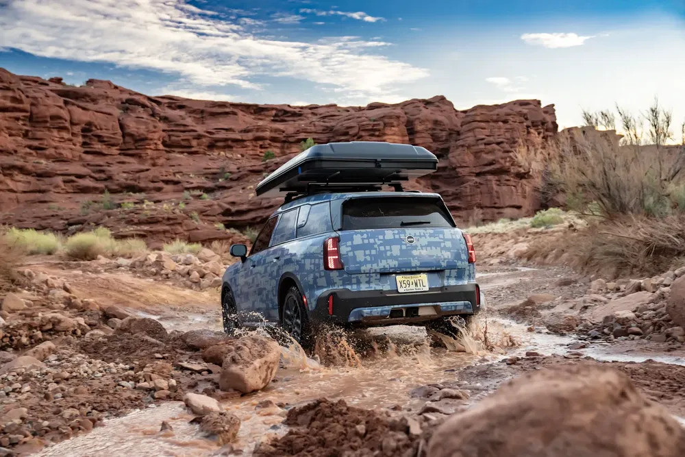 Kia EV9 off-road avontuur door rotsachtige rivier met blauwe lucht en rode rotsformaties.
