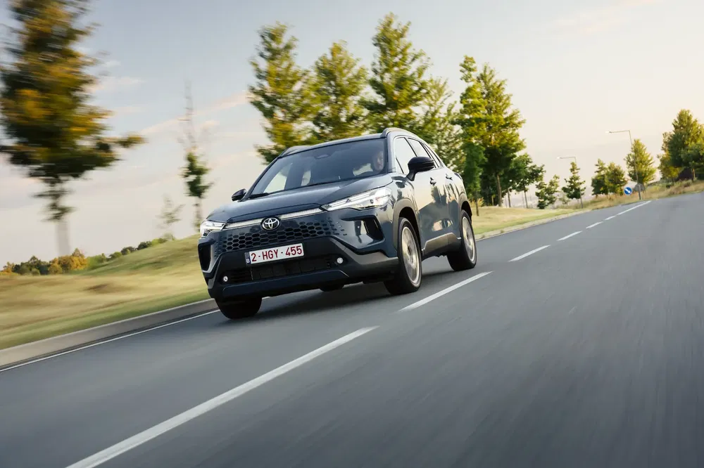 Toyota RAV4 roulant sur une route bordée d'arbres, sous un ciel dégagé.