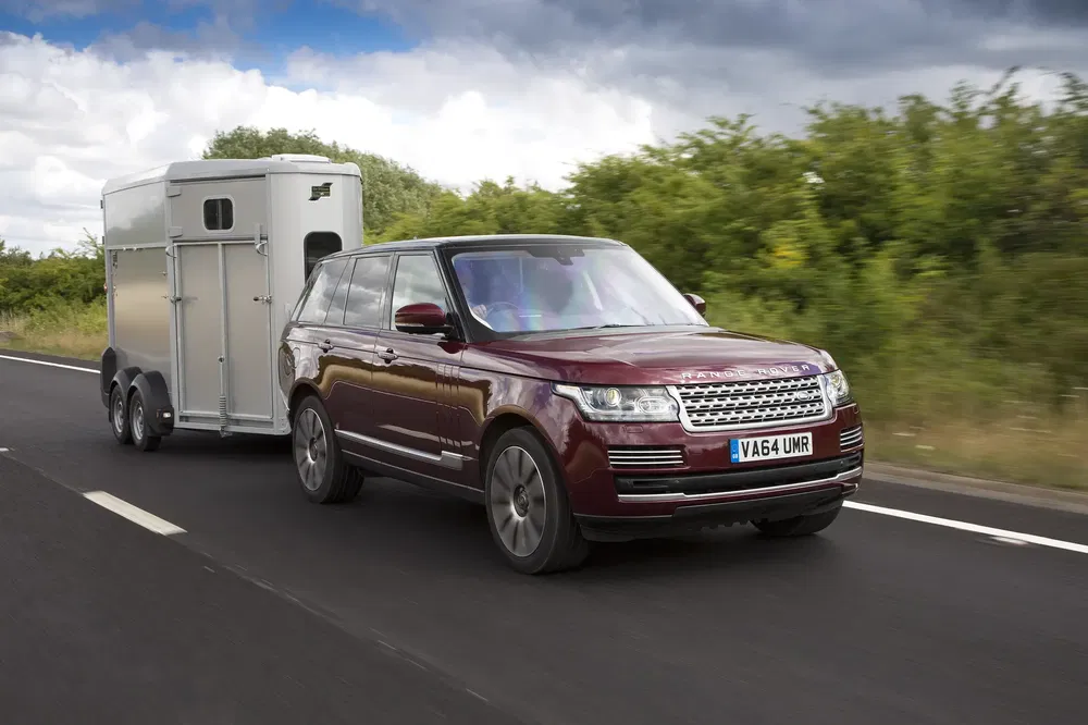 Range Rover rouge remorquant une caravane sur route bordée de végétation.