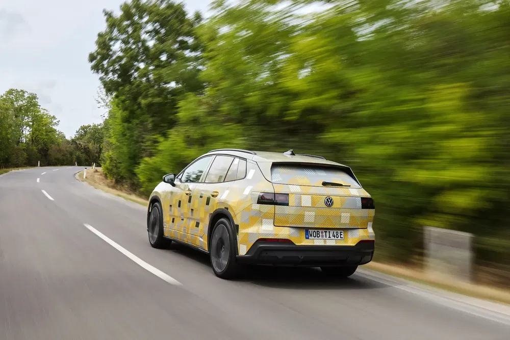 Volkswagen camouflé sur route de campagne bordée d'arbres, voiture électrique moderne.