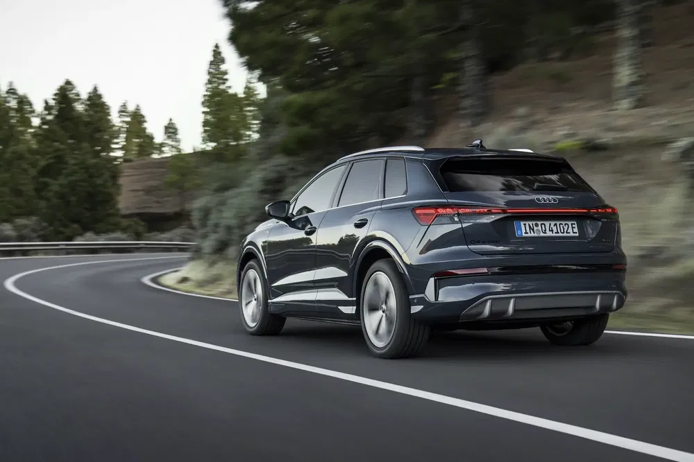 SUV Audi e-tron noir sur route sinueuse, entouré de forêt luxuriante.