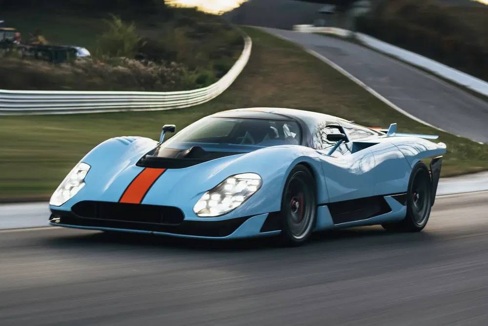Hypercar bleu ciel et orange en course sur circuit sinueux.