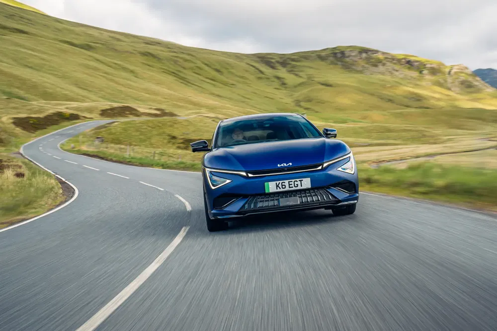 Kia EV6 GT bleu roulant sur une route sinueuse dans un paysage vallonné.