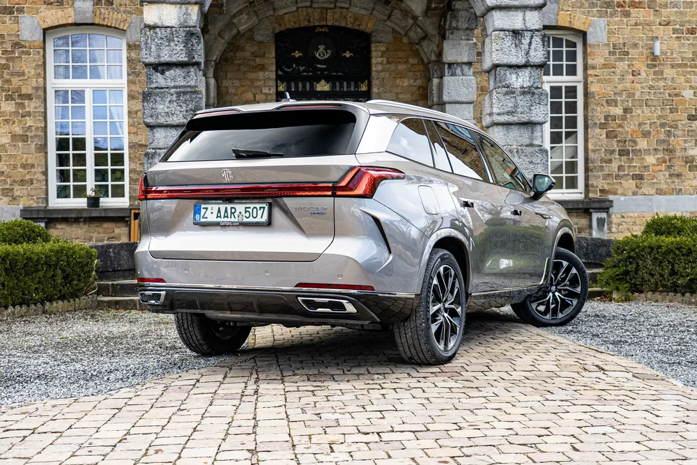 MG EHS SUV geparkeerd voor een stenen gebouw, stijlvolle achteraanzicht.