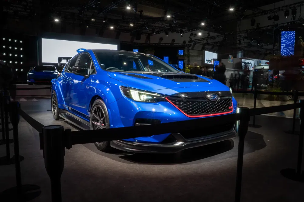 Blauwe Subaru WRX gepresenteerd op een autoshow, met sfeerverlichting en high-tech omgeving.