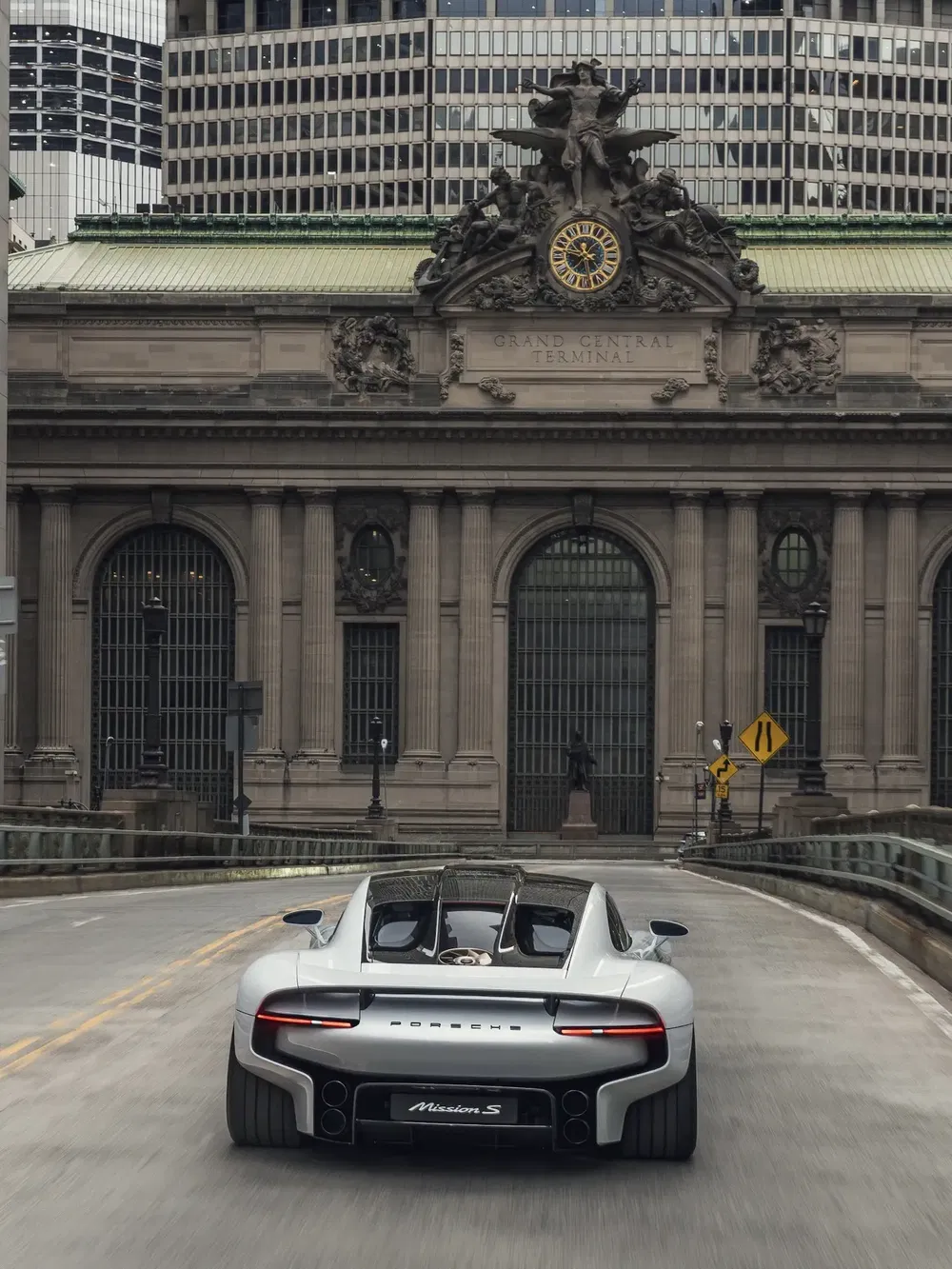 Grijze Porsche voor Grand Central Terminal, moderne auto en historische architectuur.