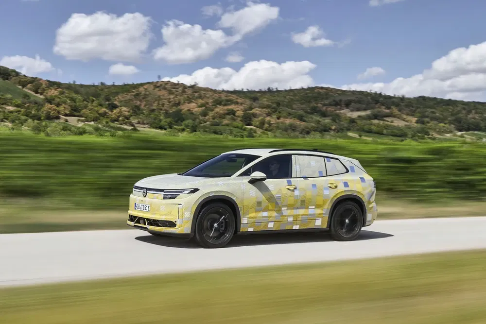 SUV Volkswagen en test, camouflé, roulant sur route panoramique sous ciel bleu.