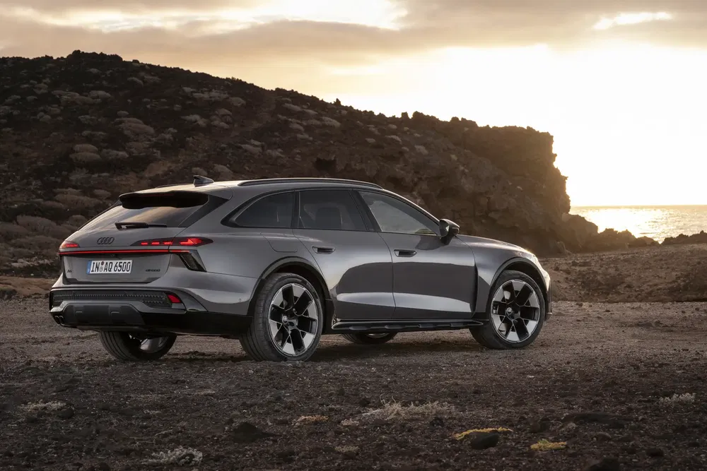 Grijze Audi A6 Allroad 2024 op rotsachtig terrein bij zonsondergang.